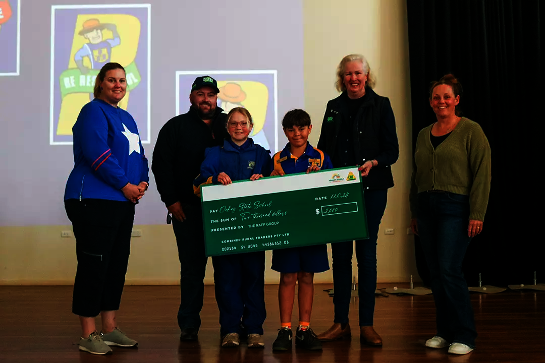 4 adults and 2 primary school students stand together on a stage holding a giant cheque